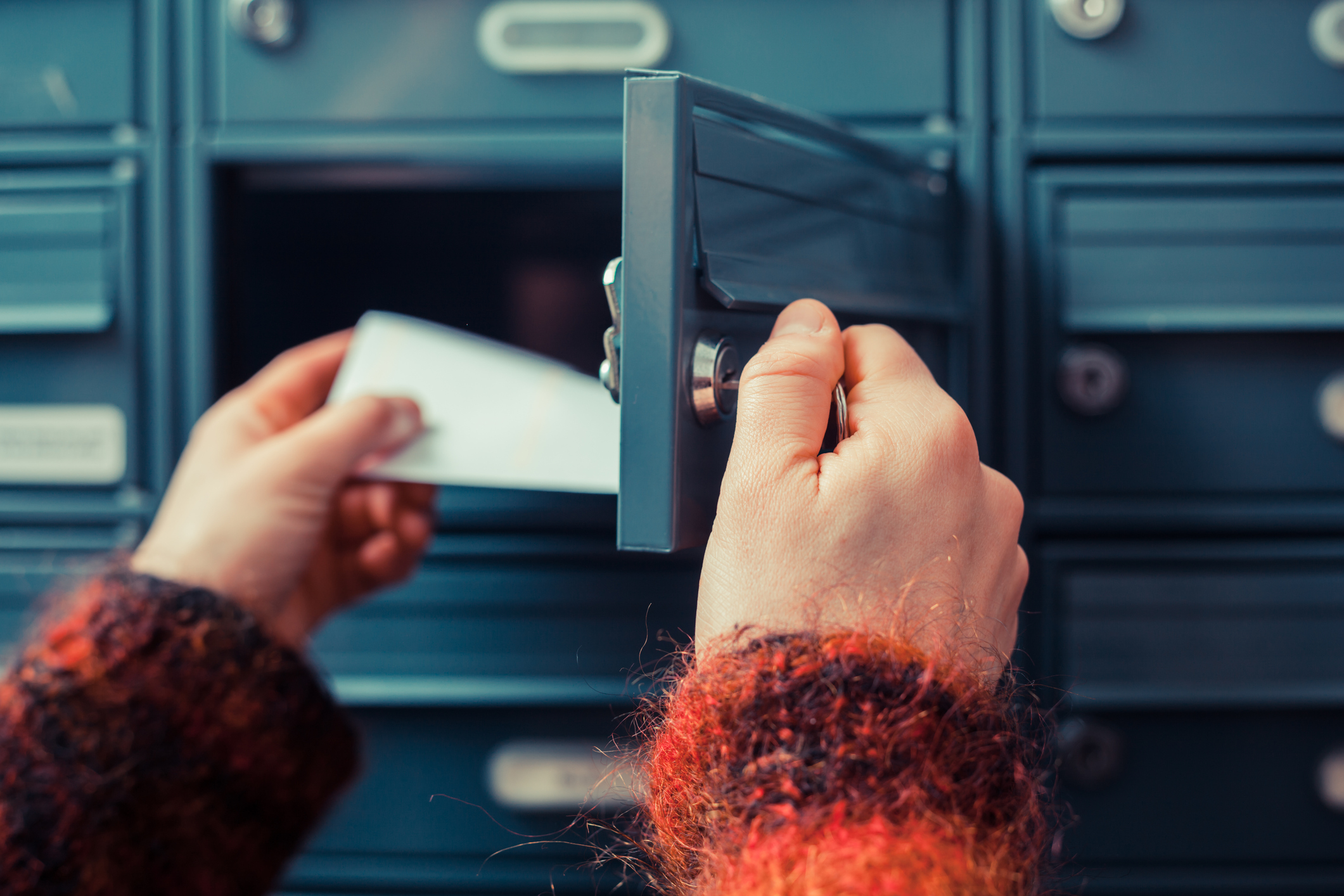 Person öffnet einen Briefkasten und nimmt Post heraus Person öffnet einen Briefkasten und nimmt Post heraus