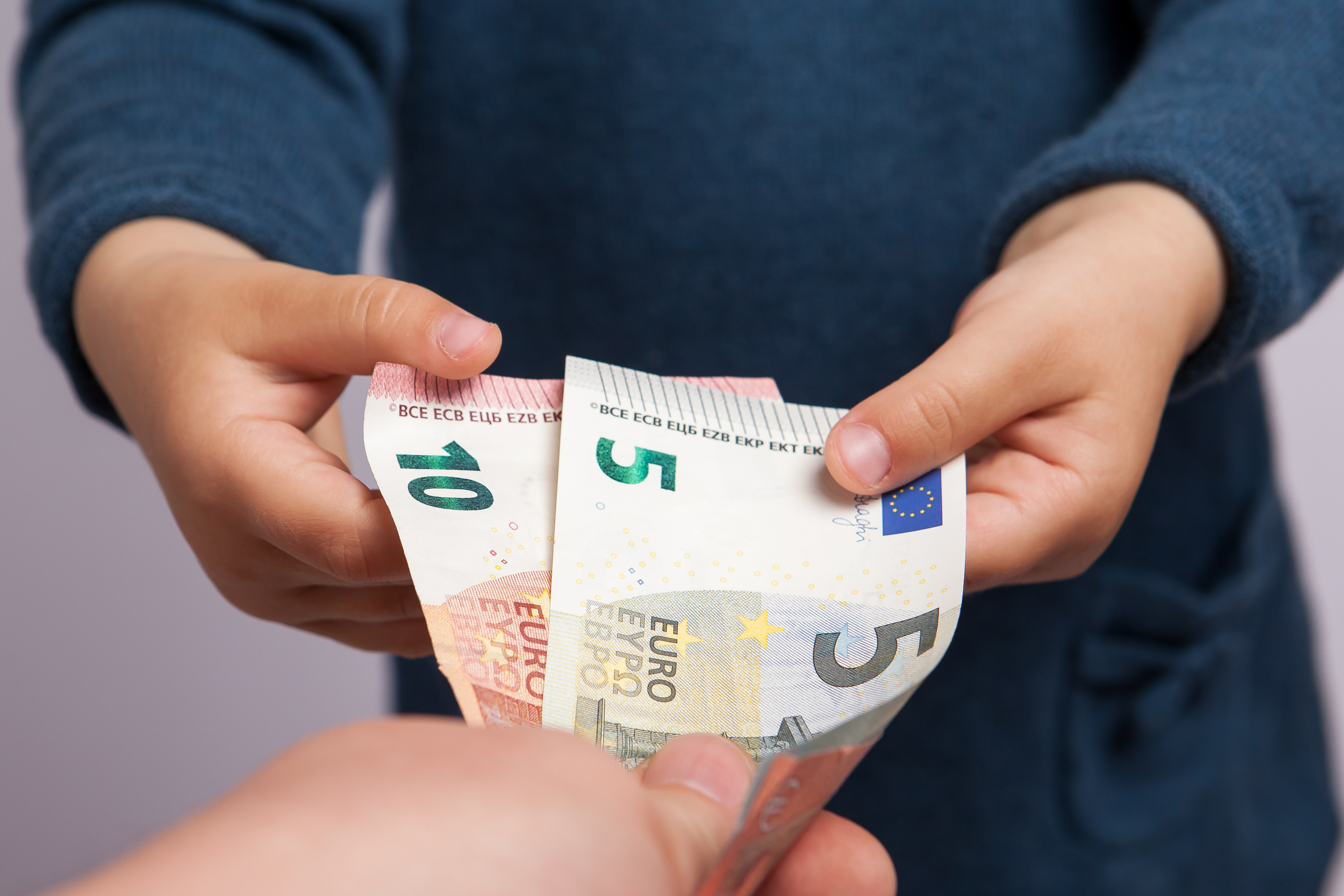 Kinderhände greifen nach Geldscheinen, die eine Hand hinhält. Kinderhände greifen nach Geldscheinen, die eine Hand hinhält.