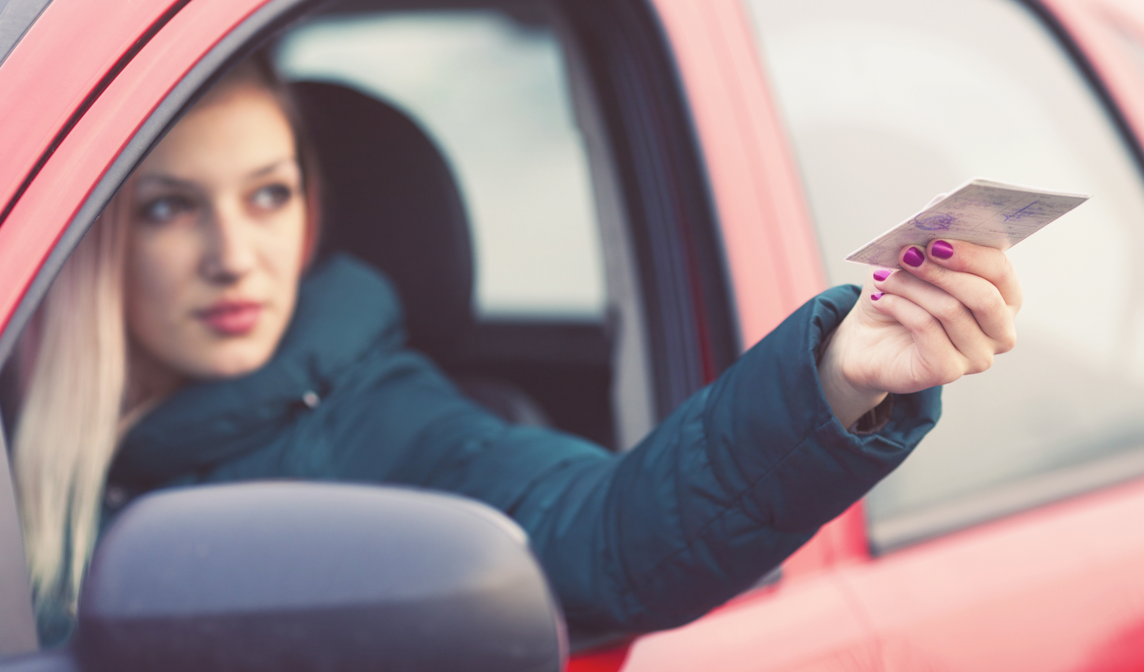 Frau sitzt im Auto und reicht Führerschein durchs Autofenster nach draußen. Frau sitzt im Auto und reicht Führerschein durchs Autofenster nach draußen.