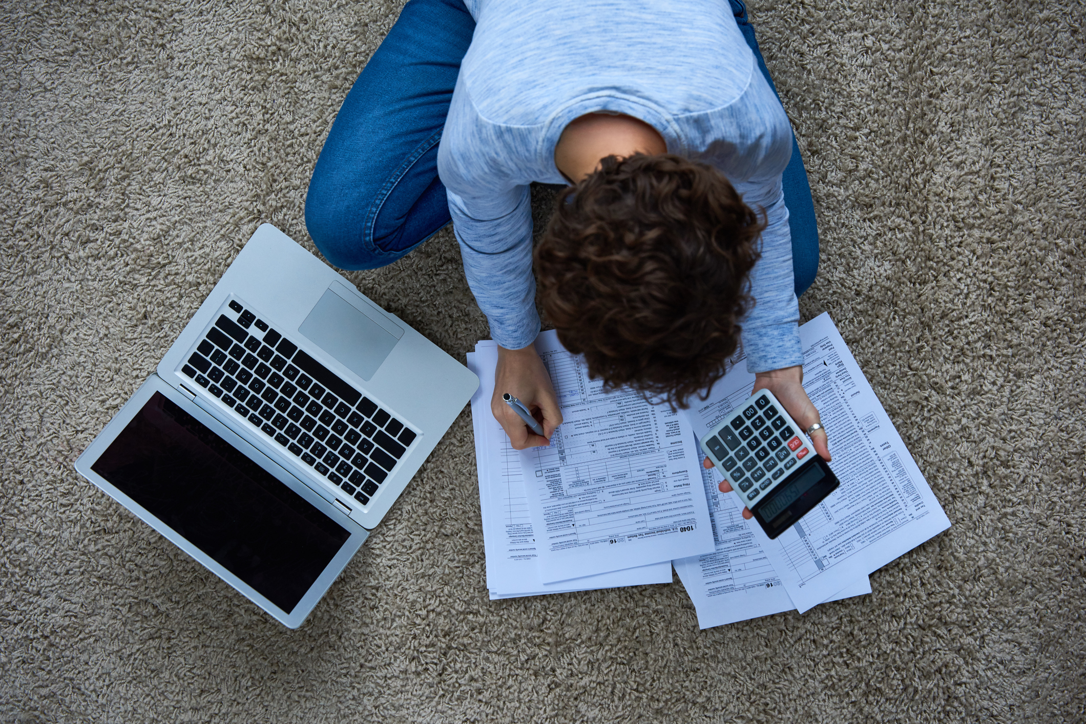 Frau sitzt auf dem Boden mit Laptop und Steuererklärung