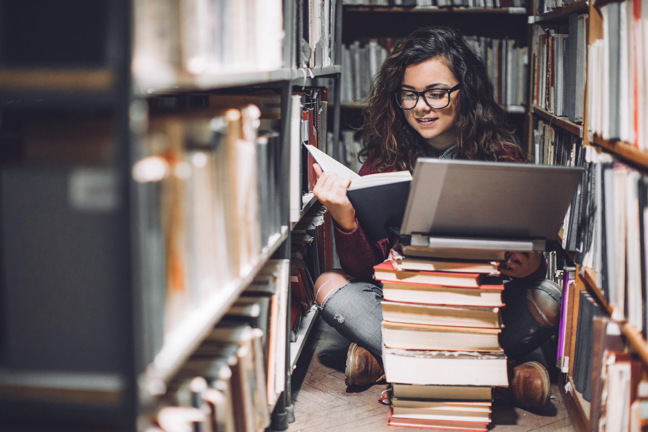 Weibliche Studentin sitzt mit Laptop auf dem Fußboden einer Bibliothek. Weibliche Studentin sitzt mit Laptop auf dem Fußboden einer Bibliothek.