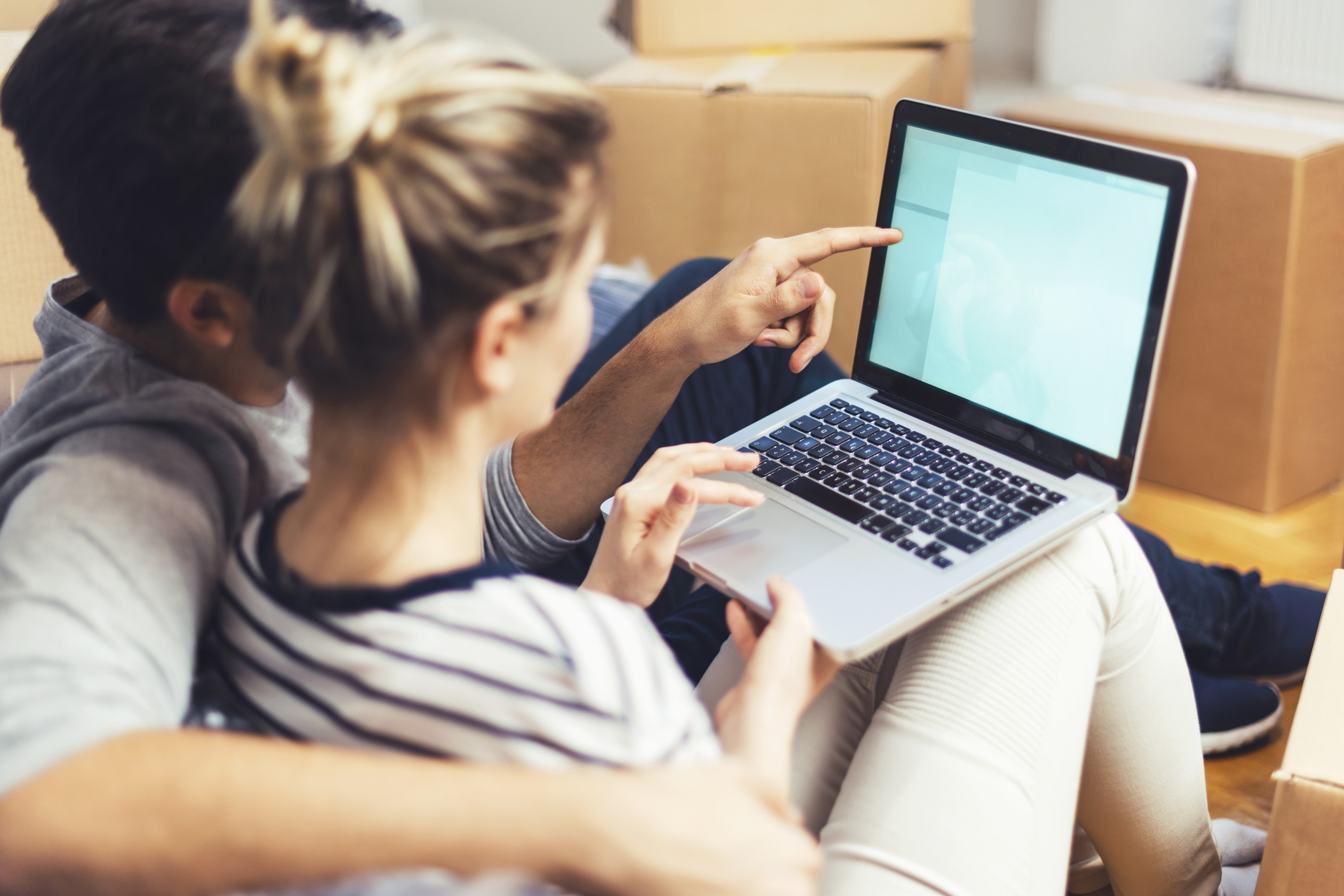 Paar sitzt zwischen Umzugskisten und schaut auf Laptop Paar sitzt zwischen Umzugskisten und schaut auf Laptop
