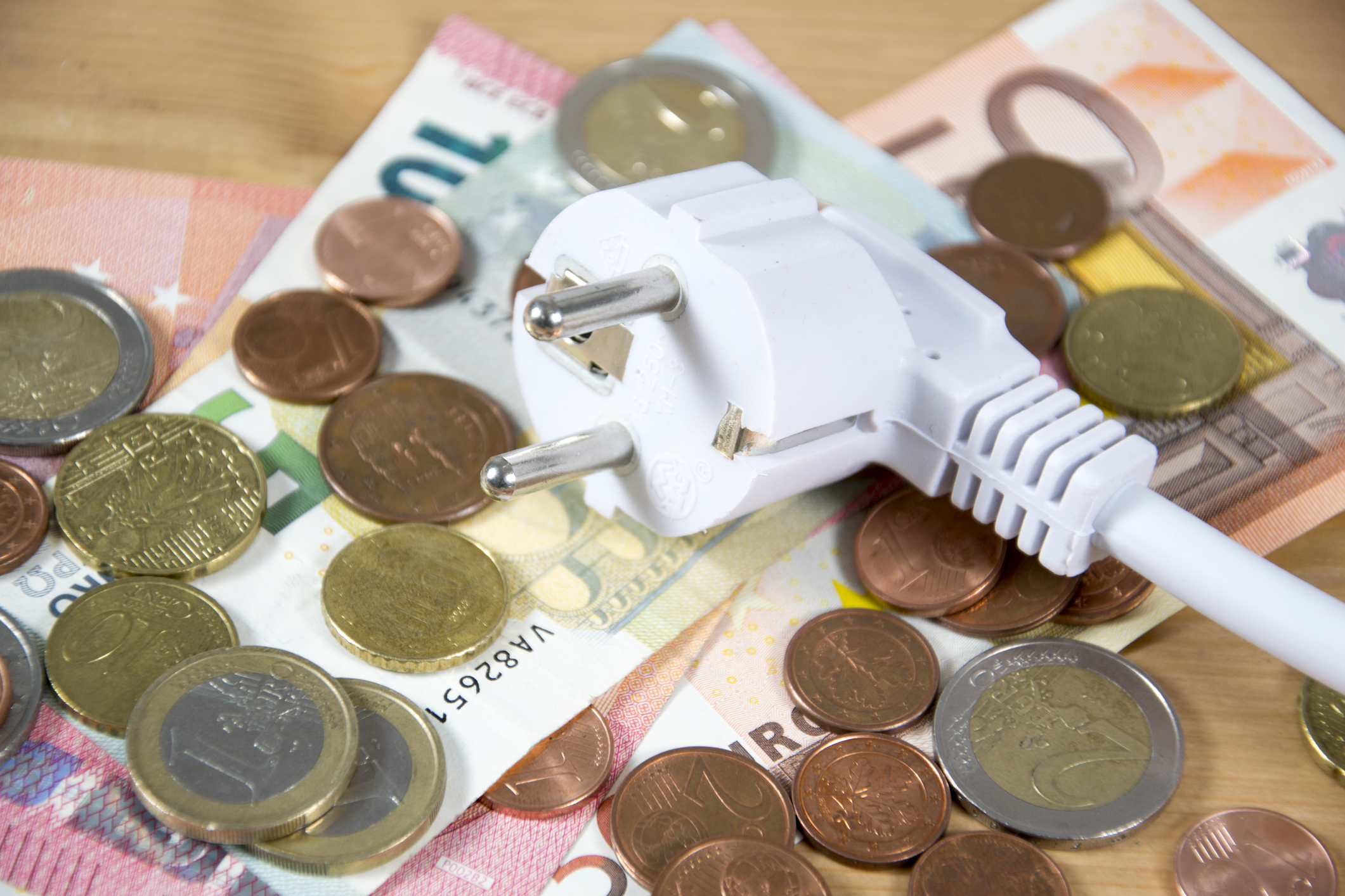 Strom anmelden: So kommt nach dem Umzug Energie ins Haus Geldscheine und Kleingeld, auf denen ein Stromstecker liegt.