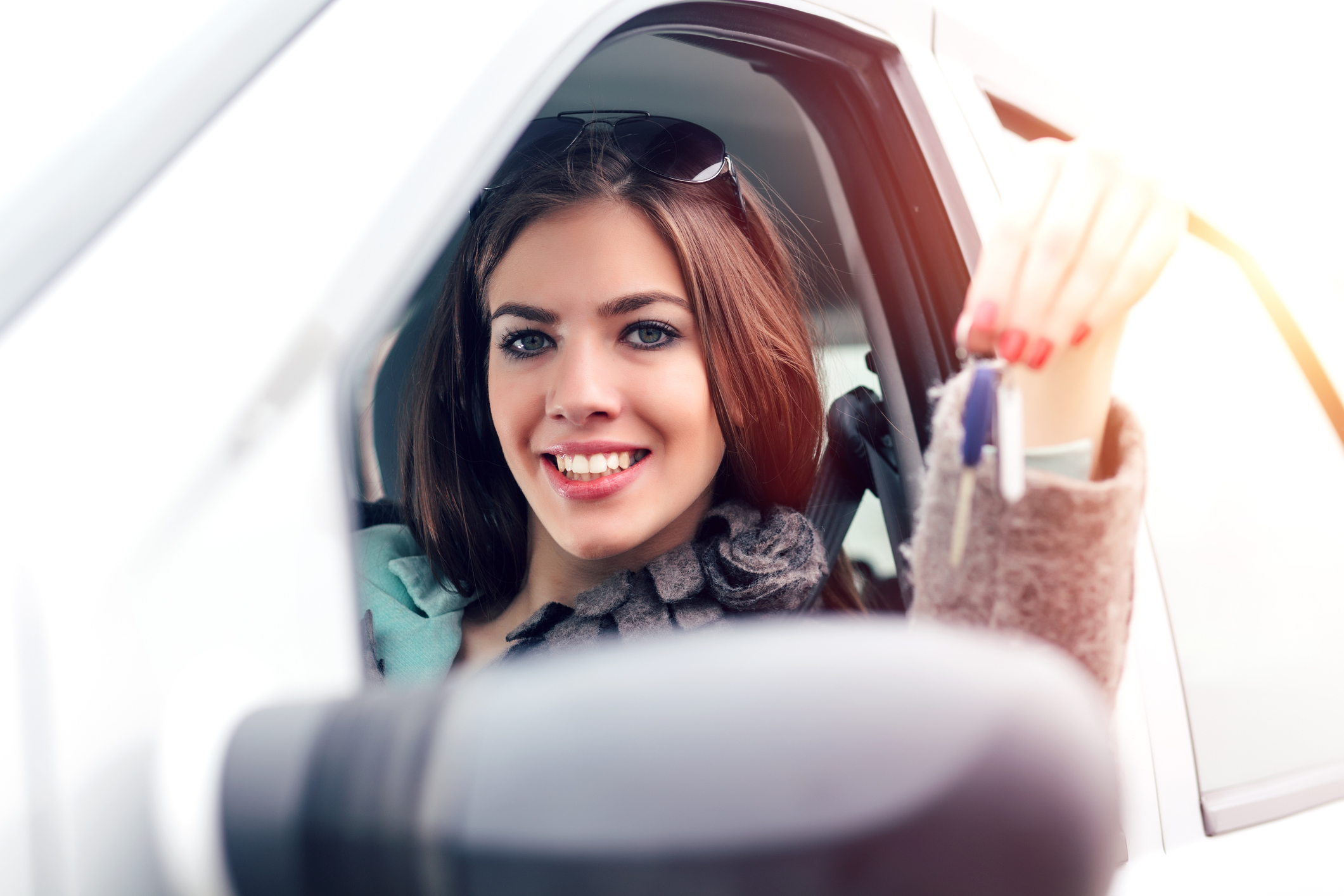 Kfz-Halterwechsel: Was beim Auto-Ummelden wichtig ist Junge Frau sitzt am Steuer und zeigt Autoschlüssel