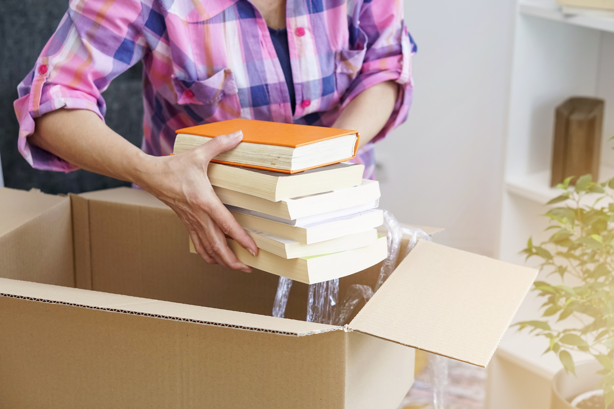 Kisten & Kosten: Wie viele Umzugskartons brauche ich? Frau packt Bücher in Umzugskarton.