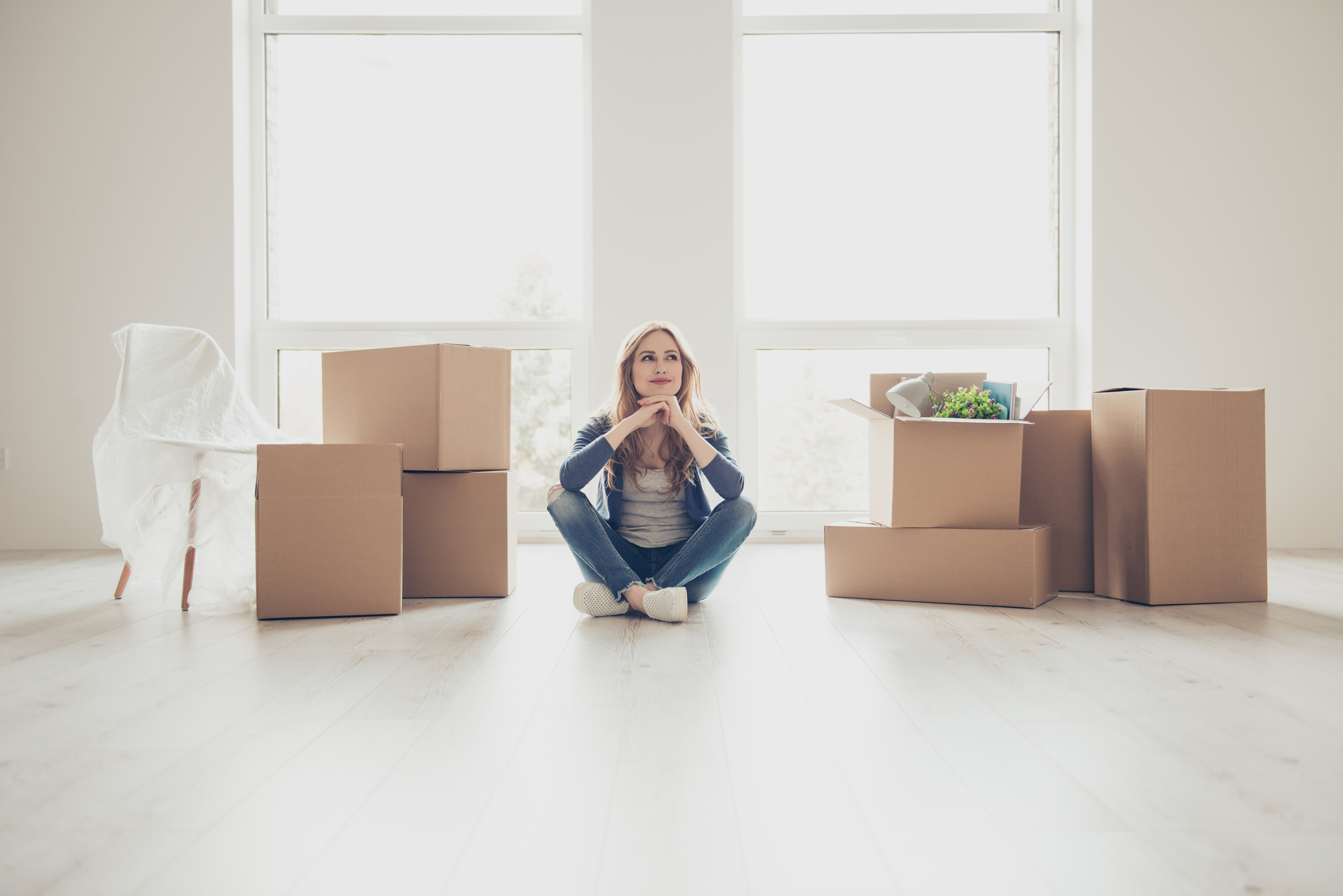 Kaution versus Genossenschaftsanteile: Was ist der Unterschied? Junge Frau sitzt in leerer Wohnung, Umzugskartons stehen neben ihr.