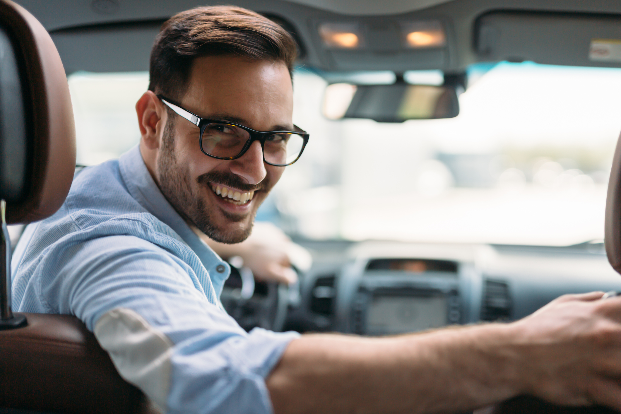Kfz & Auto ummelden nach dem Umzug: Kosten & Tipps Mann sitzt lächelnd im Auto und schaut nach hinten