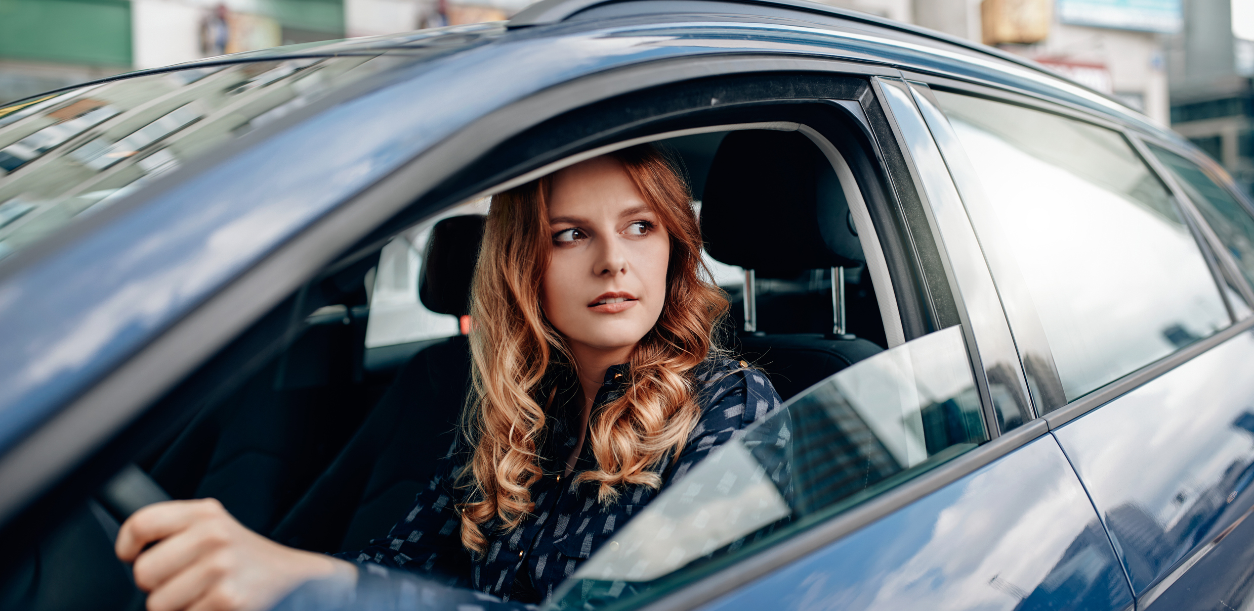 Kfz-Versicherung wechseln: Wann und wie geht das? Junge Frau am Steuer eines Autos schaut aus dem Fenster