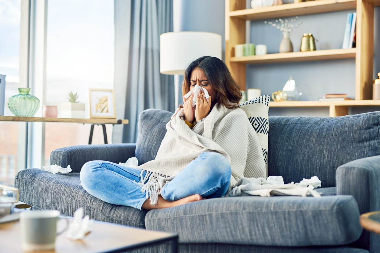 Plötzliche Allergie in der neuen Wohnung Frau putzt sich die Nase auf Sofa