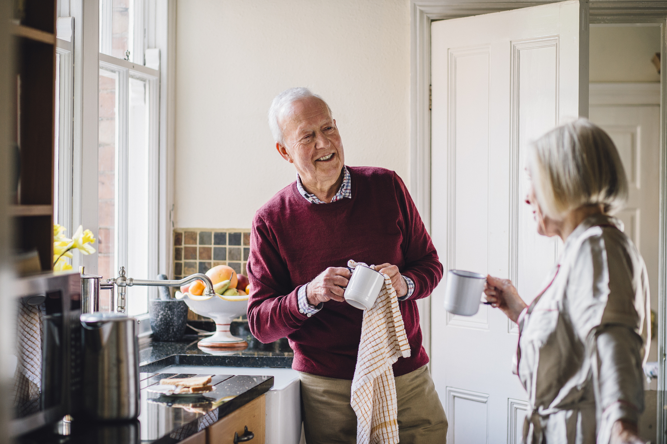 Senioren-WG: Modernes Lebenskonzept für Rentner und Best-Ager 50+ Älterer Mann trocknet Kaffeebecher mit kariertem Geschirrtuch ab