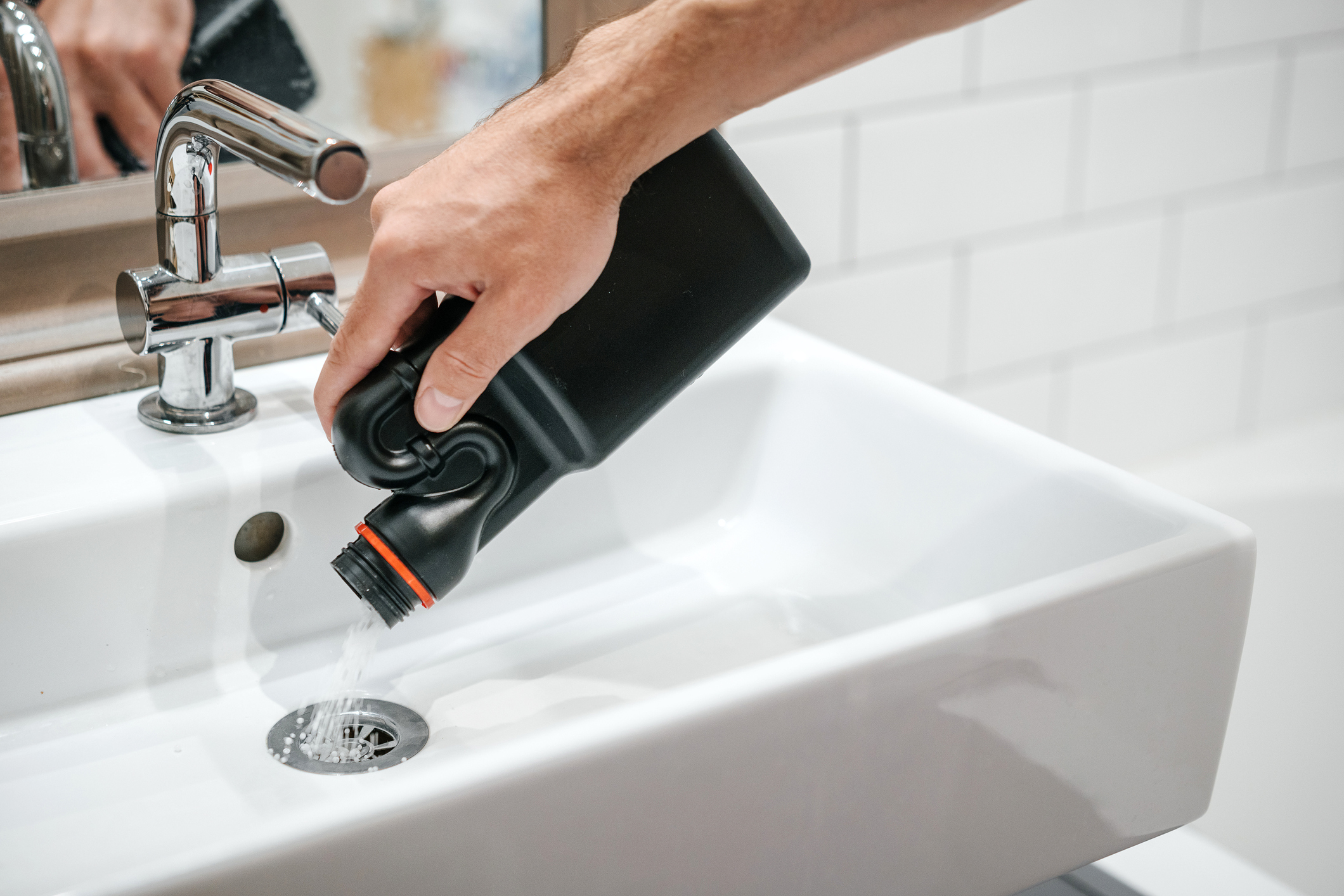 Siphon reinigen: Verstopften Abfluss selbst reparieren Mann schüttet Rohrreiniger in den Ausguss eines Waschbeckens