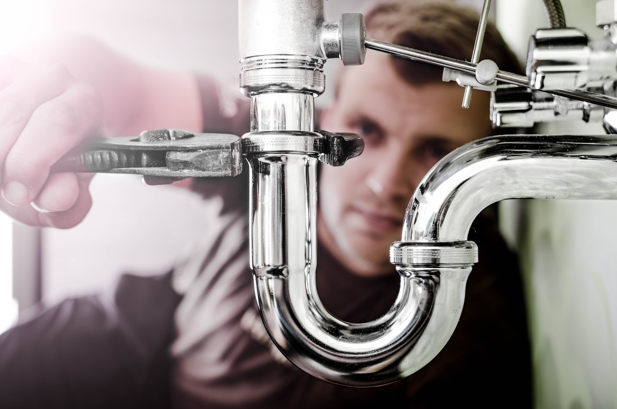 Siphon reinigen: Verstopften Abfluss selbst reparieren Mann schraubt mit einer Zange den Metallsiphon eines Waschbeckens ab