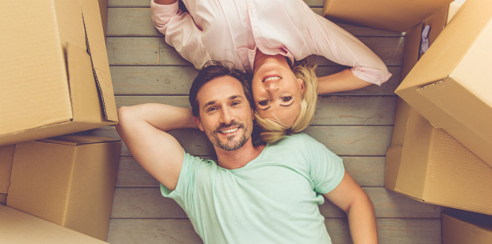 Sonderurlaub Mann und Frau liegen zwischen Umzugskartons auf dem Fußboden und schauen lächelnd nach oben