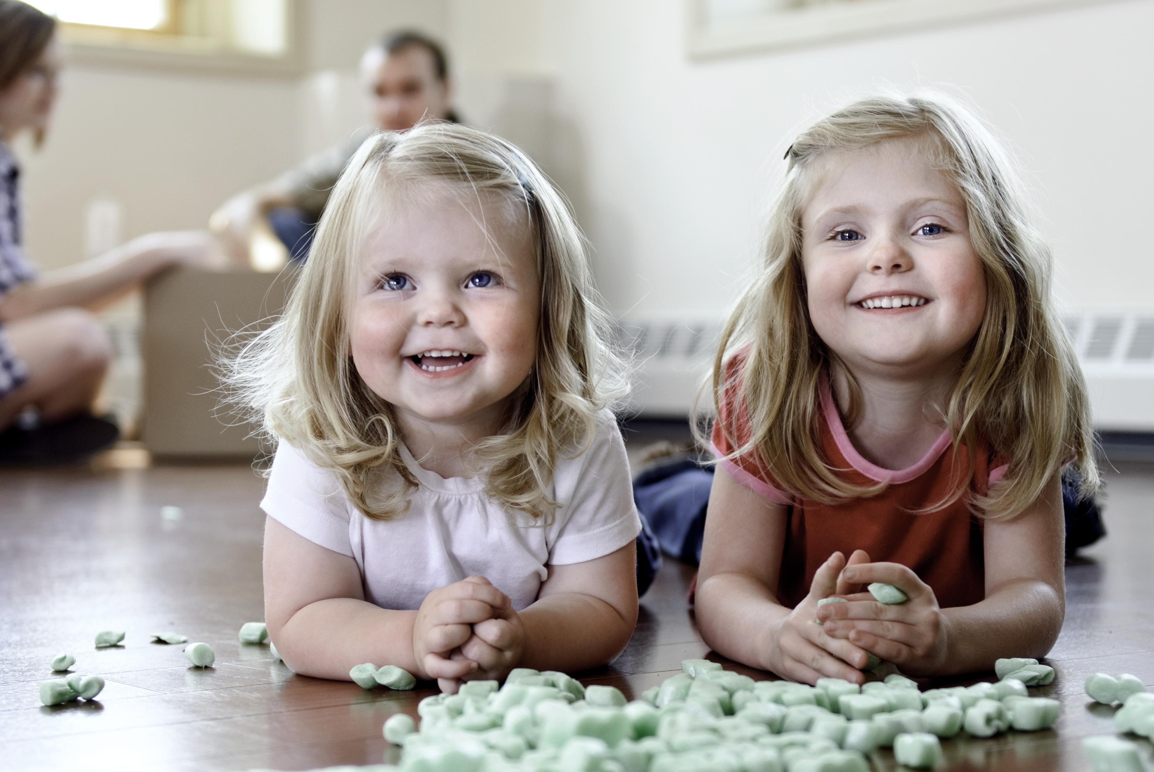 So klappt der Umzug mit Kindern ganz entspannt Kleine Mädchen spielen mit Verpackungsmaterial, im Hintergrund die Eltern mit