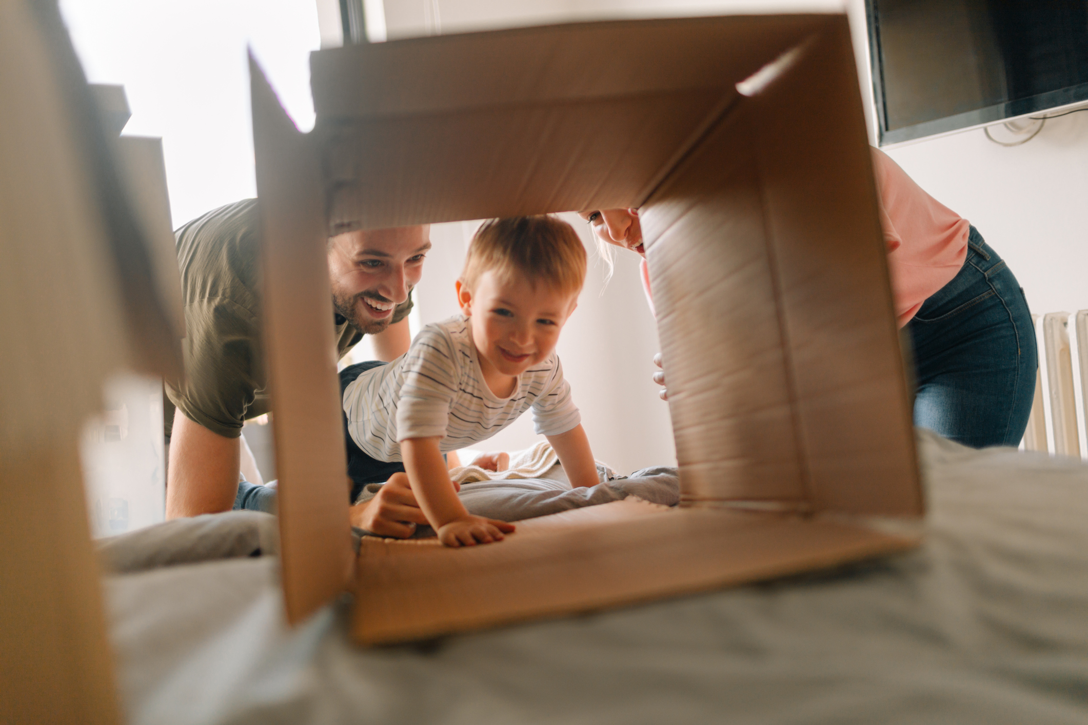 Umzug planen: Tipps für den DIY-Umzug Lachende Familie mit Kleinkind, das in einen Umzugskarton krabbelt