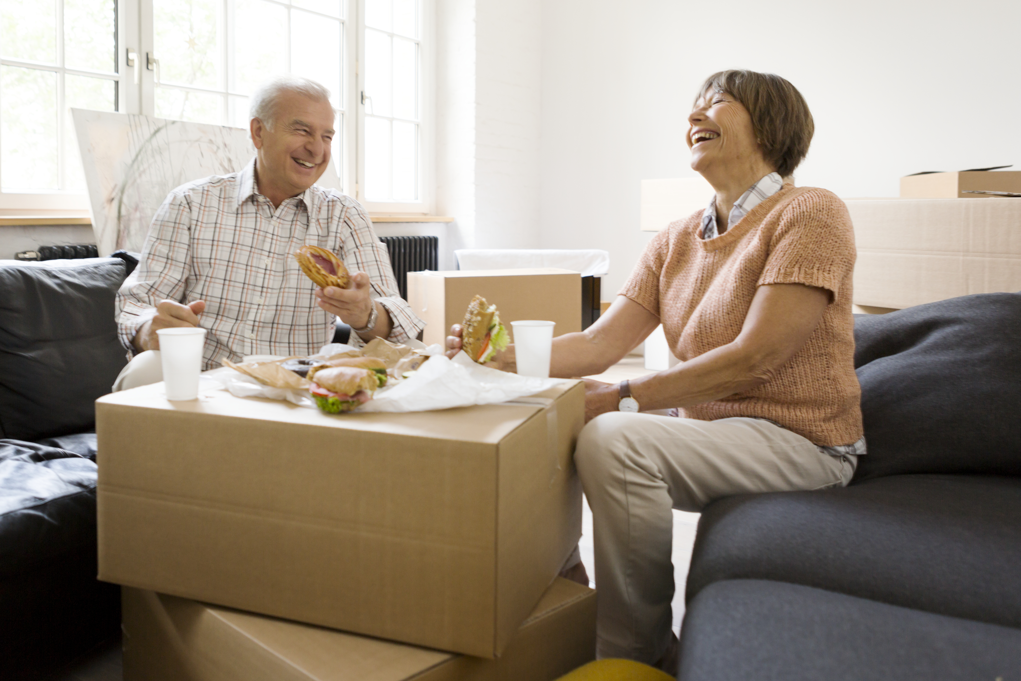 Essen für Umzugshelfer: Verpflegung für den großen Tag Älteres Paar sitzt zwischen Umzugskartons, darauf belegte Brote.