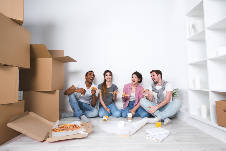 Umzugshelfer motivieren: So sorgen Sie am Umzugstag für beste Laune Umzugshelfer sitzen auf dem Boden und essen Pizza