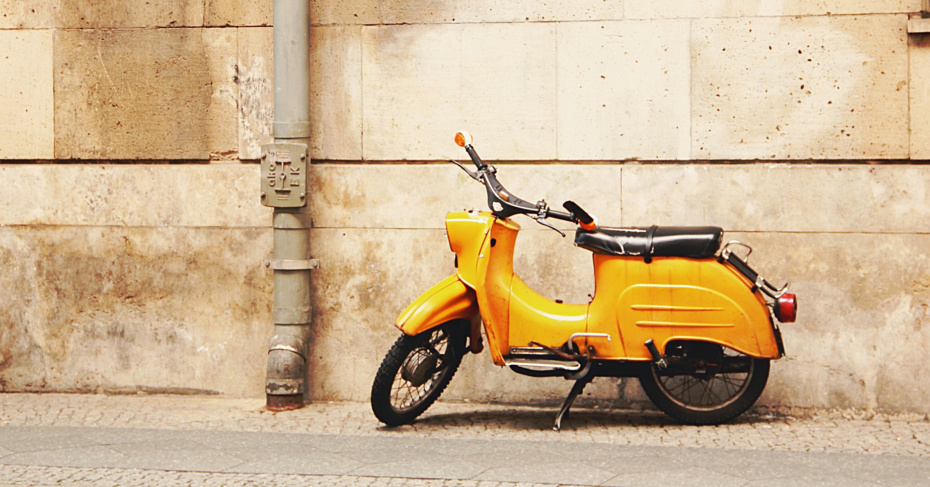 Versicherungskennzeichen: Roller, Mofa & Co. anmelden Alter, gelber Roller vor einer Sandsteinmauer