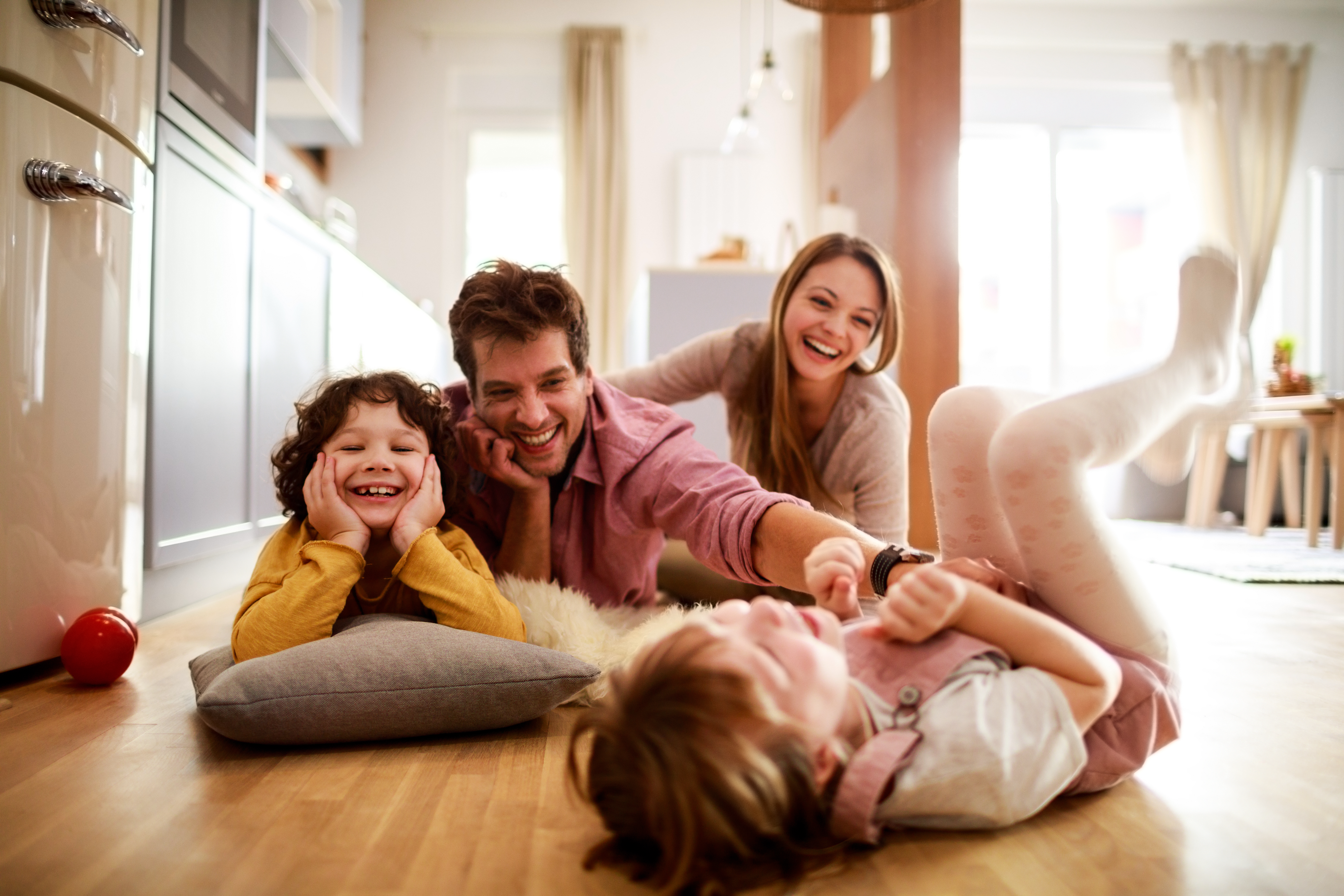 Welche Versicherungen braucht man wirklich? Junge Familie spielend und lachend auf dem Boden ihrer Wohnung
