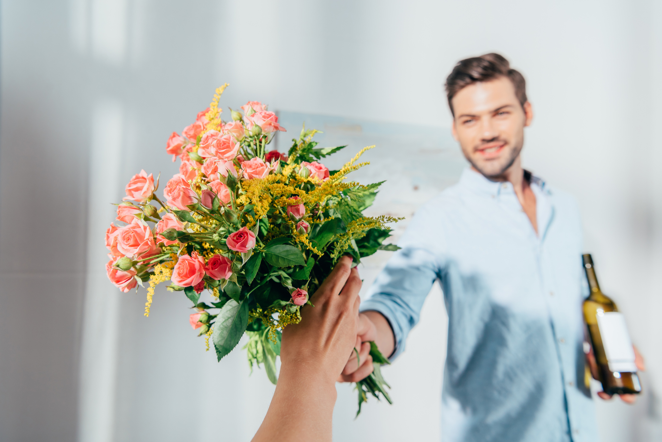 Junger Mann überreicht Frau Blumen und Wein.