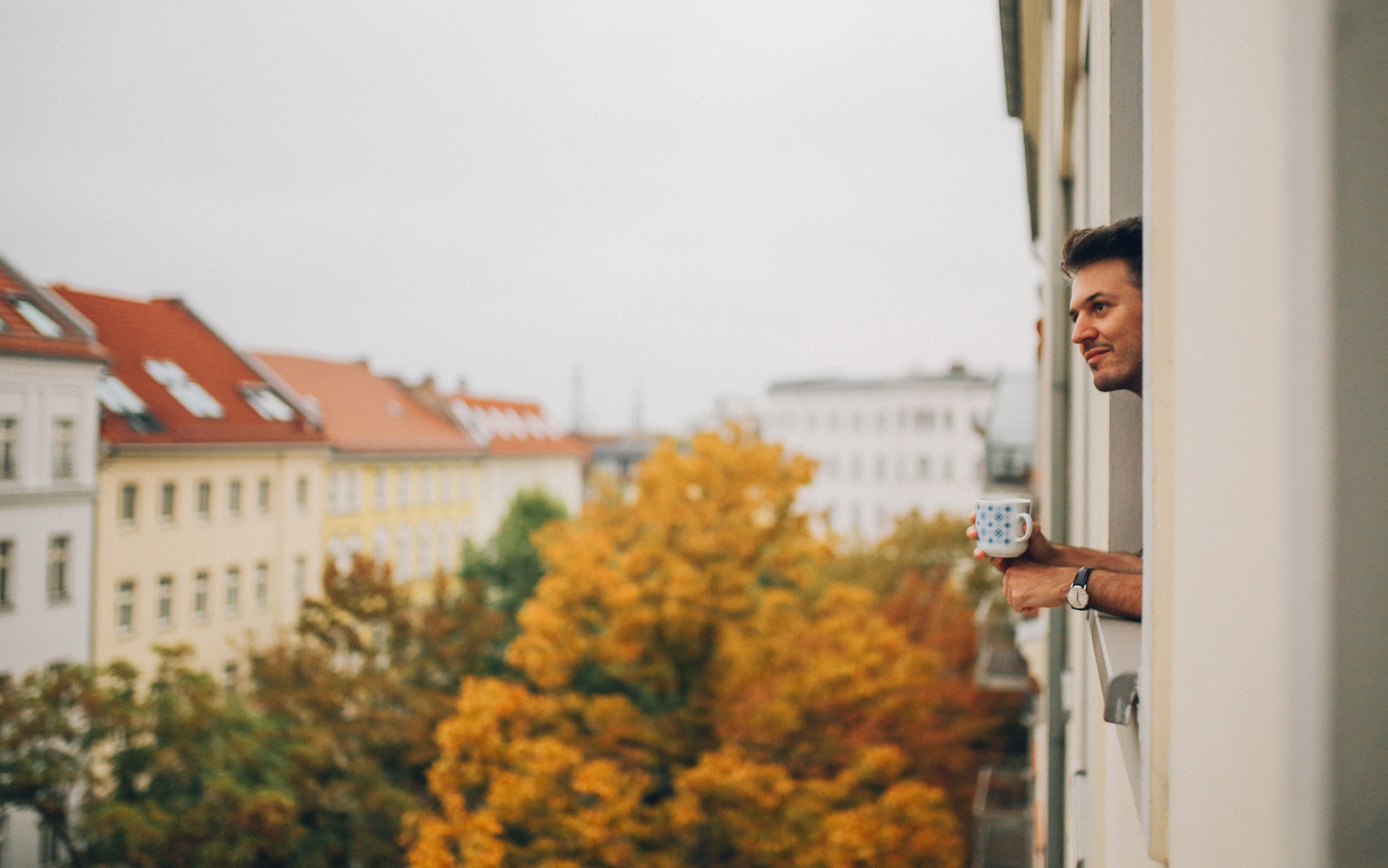 Zweitwohnsitz anmelden: Meldepflicht für den Nebenwohnsitz Junger Mann schaut aus dem Fenster eines größeren Wohnhauses