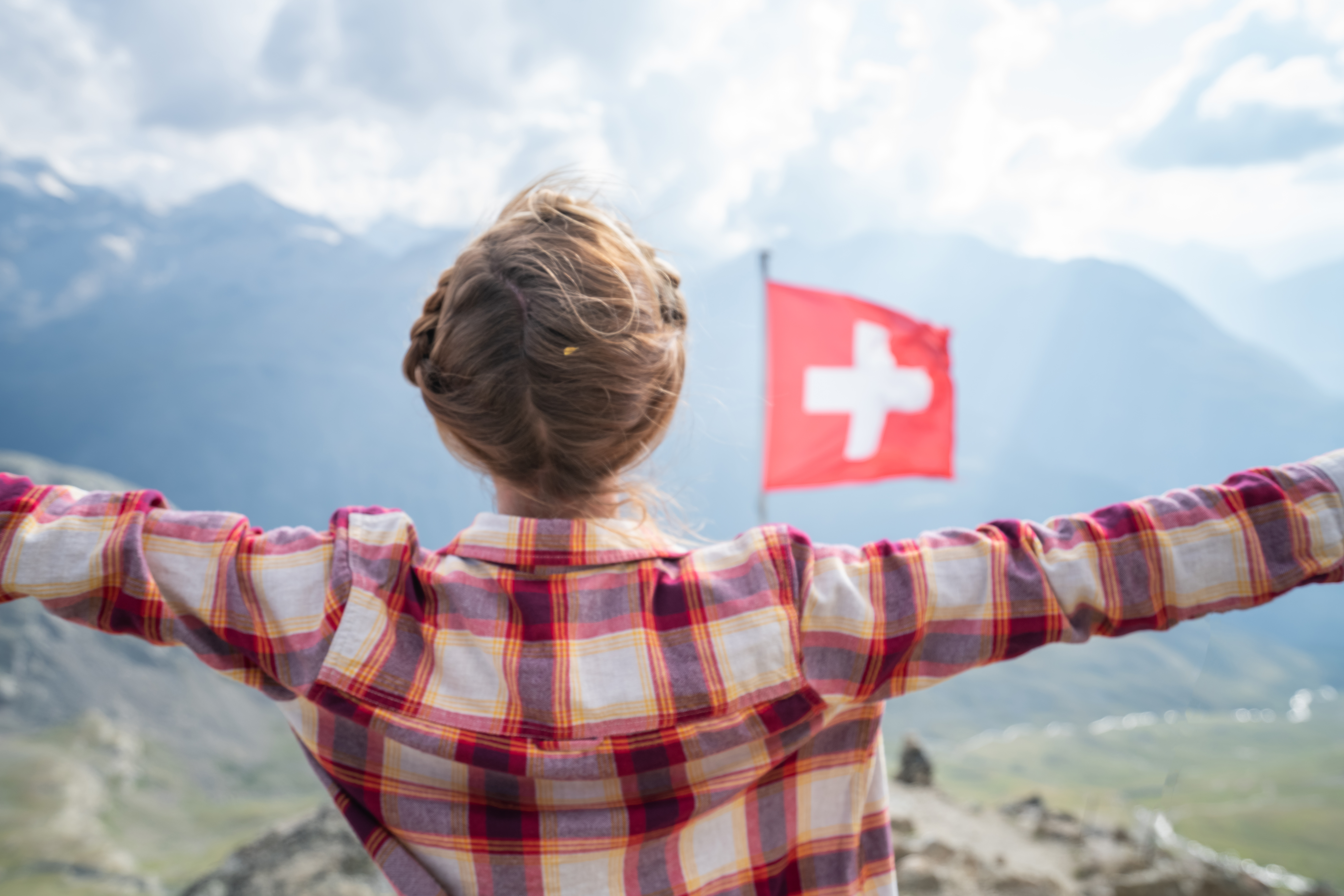 Auswandern in die Schweiz: Wissenswertes für Umzugswillige Frau am Matterhorn mit Schweizer Flagge