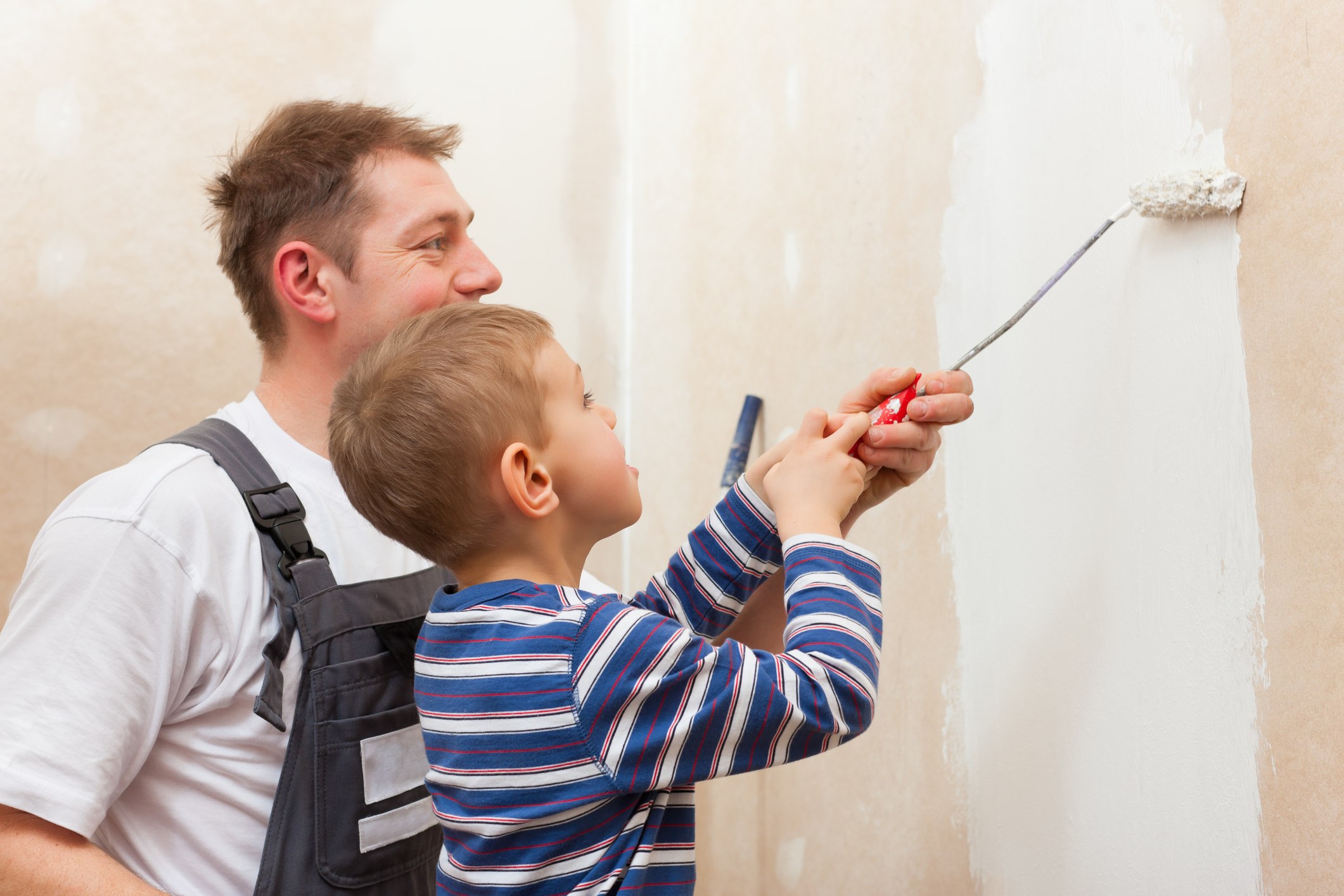Schönheitsreparaturen: Ein Mann und ein junge streichen gemeinsam eine Wand. Schönheitsreparaturen: Ein Mann und ein junge streichen gemeinsam eine Wand.