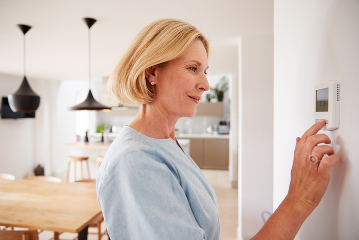 Energieausweis beantragen: Was muss ich wissen? Frau steht vor einem Heizungsthermostat