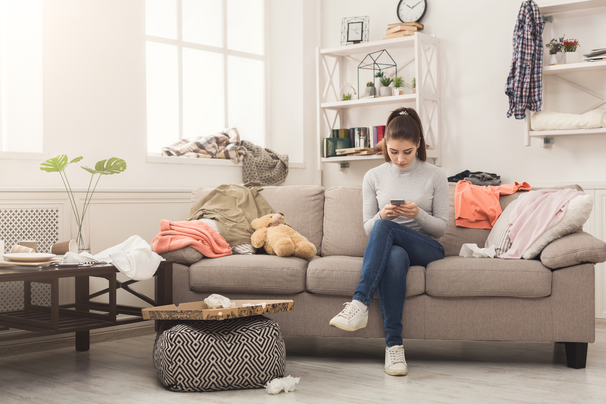 Die erste gemeinsame Wohnung: Umzugstipps fürs Zusammenziehen Junge Frau sitzt in chaotischem Wohnzimmer auf der Couch
