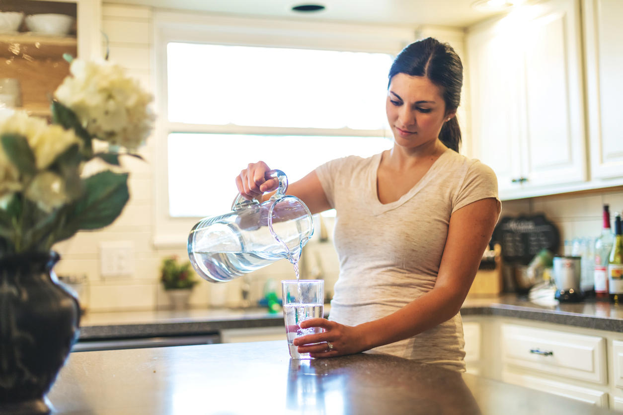 Frau schüttet Trinkwasser aus Karaffe in Glas