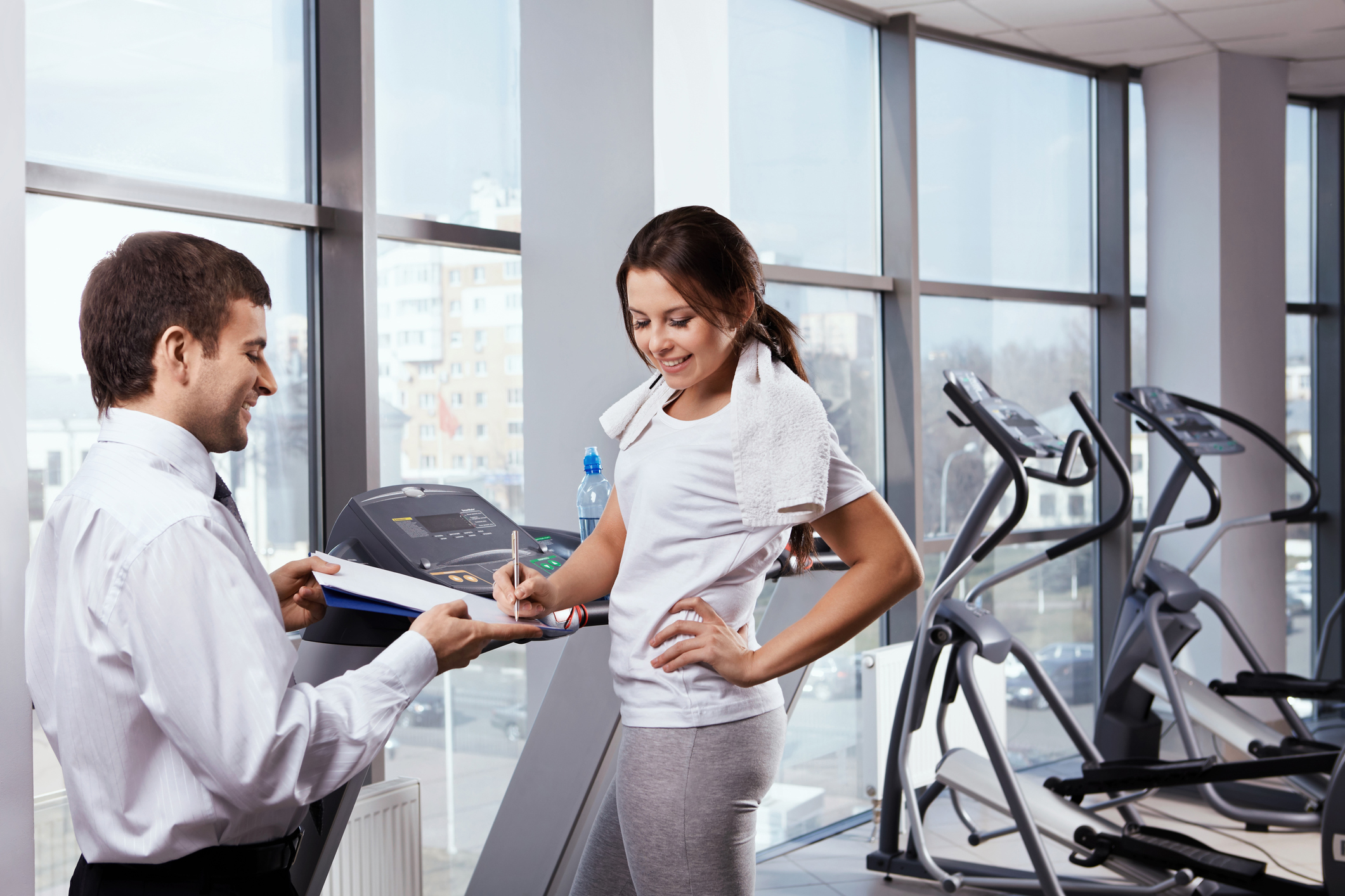 Fitnessstudio kündigen wegen Umzug: Ihre Rechte Junge Frau trainiert im Fitnessstuidion und unterschreibt ein Dokument