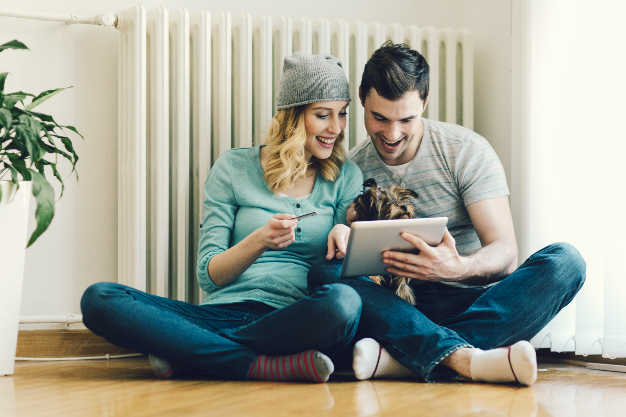Junges Paar sitzt mit Tablet-PC vor einem Heizkörper