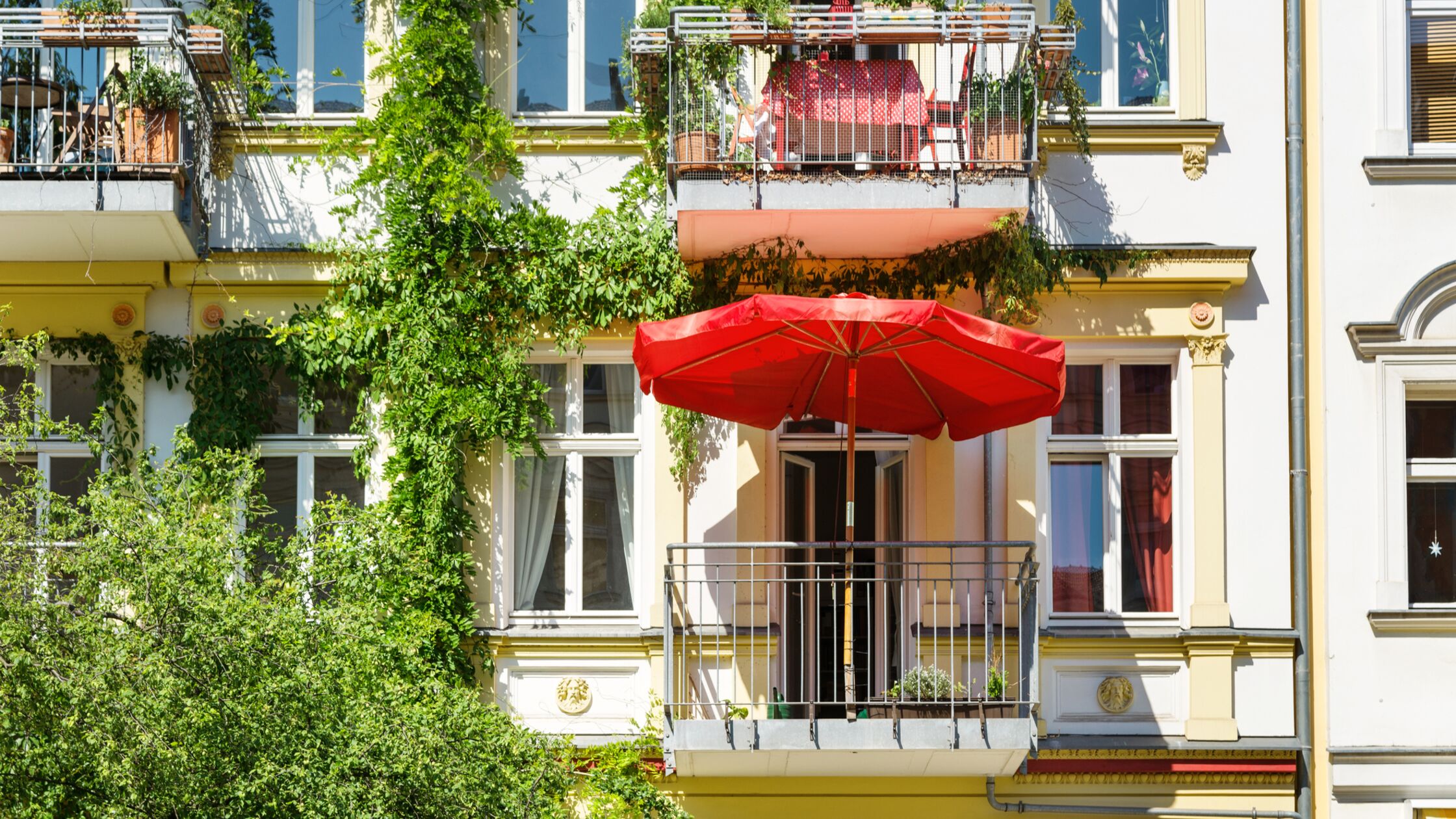 Außenansicht eines größeren Mietshauses mit bepflanzten Balkons und Sonnenschirm