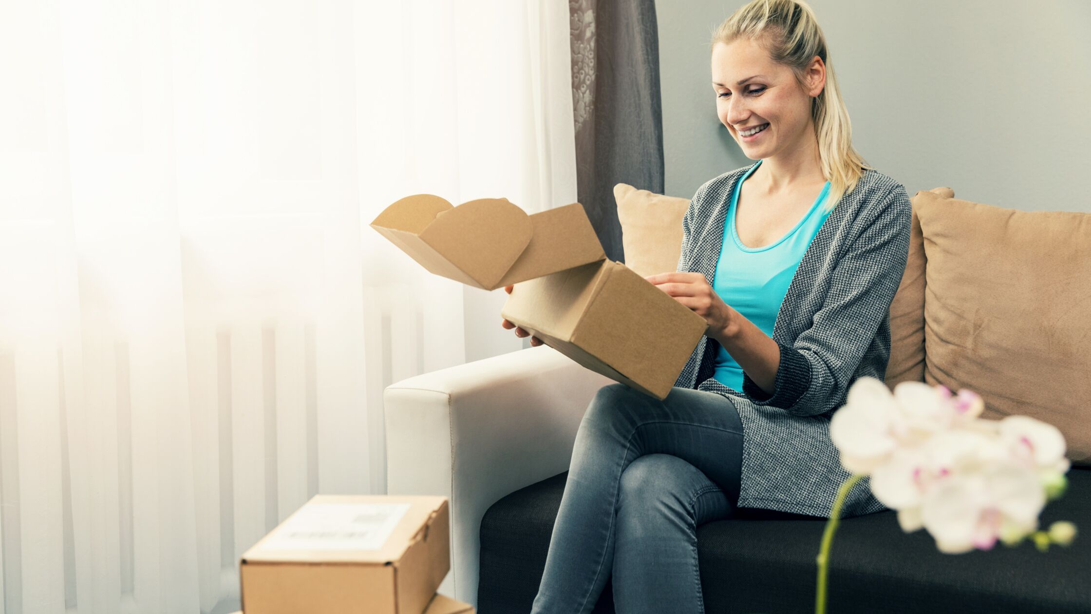 Junge Frau sitzt auf dem Sofa und öffnet Postpakete. Junge Frau sitzt auf dem Sofa und öffnet Postpakete.