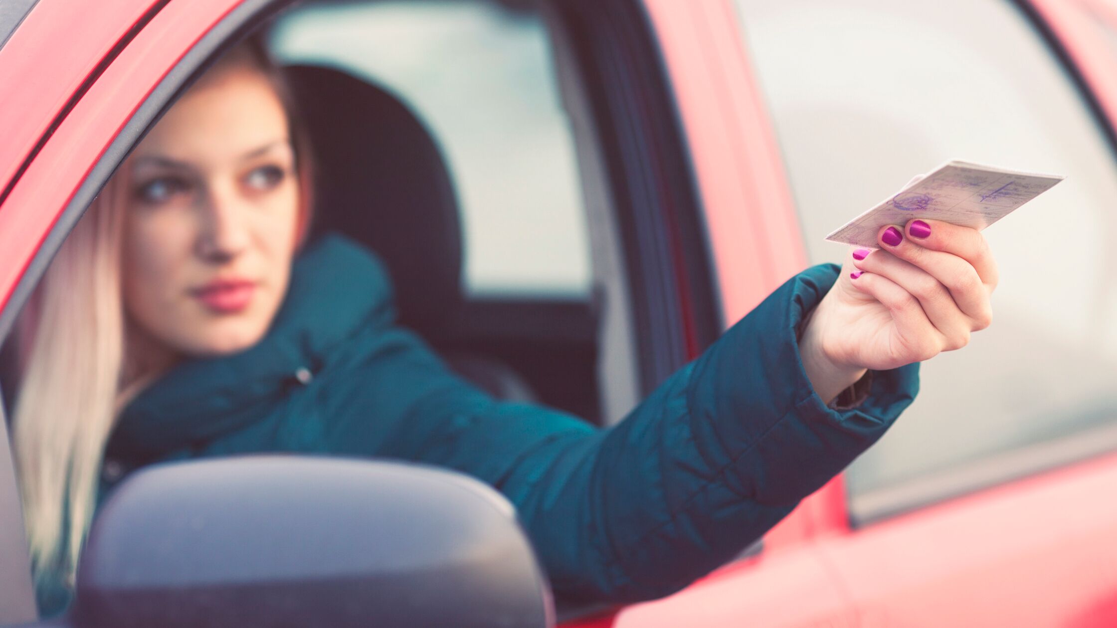 Frau sitzt im Auto und reicht Führerschein durchs Autofenster nach draußen.