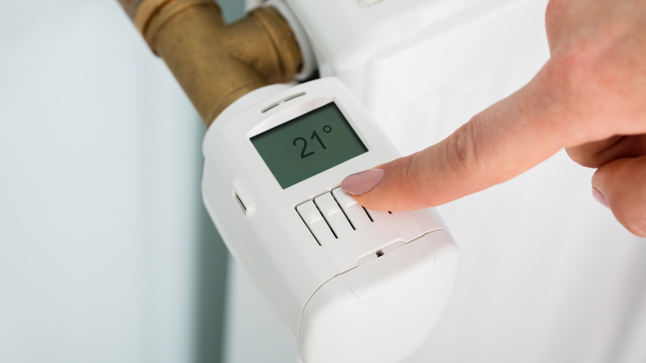 Hand mit Thermostat an einem Heizkörper, der 21°C anzeigt