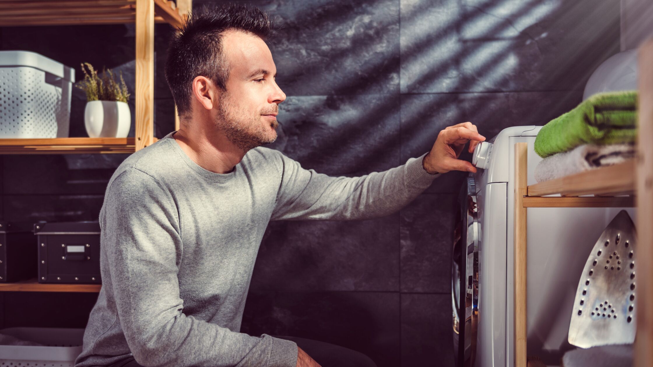 Mann kniet vor einer Waschmaschine und stellt Temperatur ein.