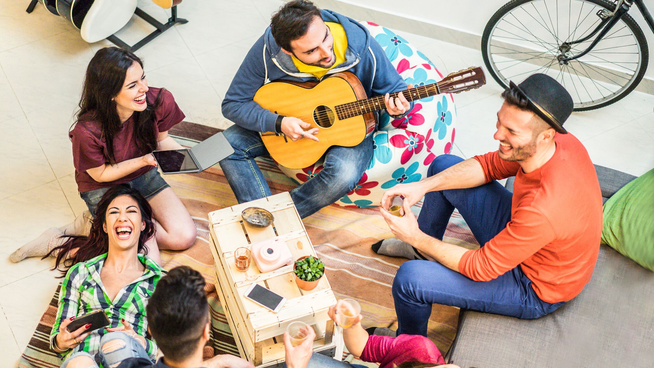 Gruppe junger Leute sitzt auf dem Boden einer Wohnung, lacht und macht Musik