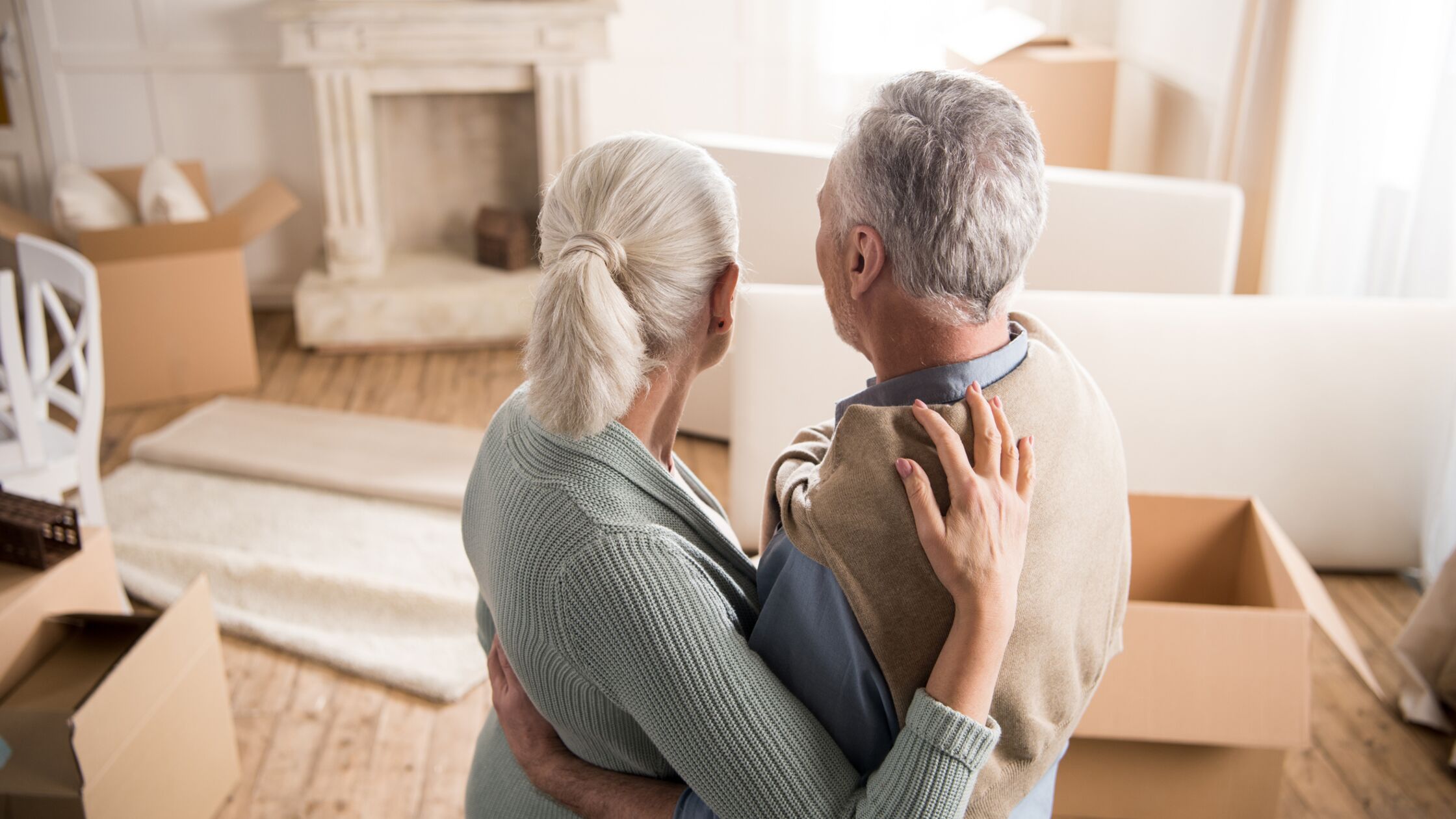 Älteres Paar umarmt sich und blickt auf ausgeräumtes Haus