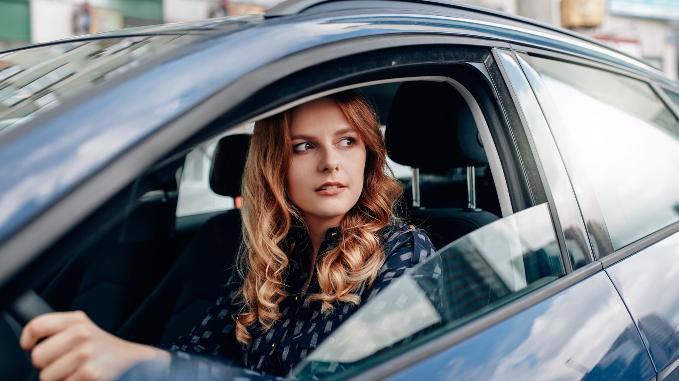 Junge Frau am Steuer eines Autos schaut aus dem Fenster