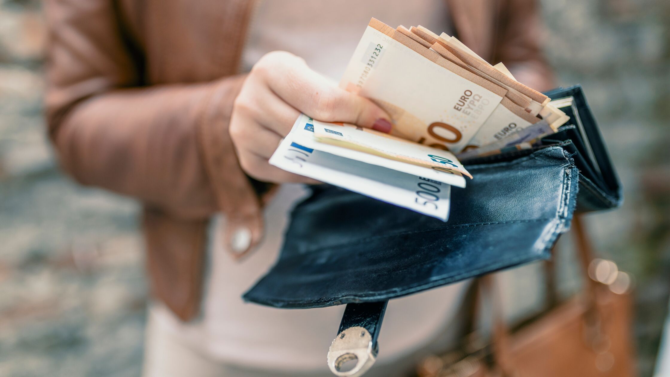 Frauenhand nimmt ein Bündel Geldscheine aus einem Geldbeutel