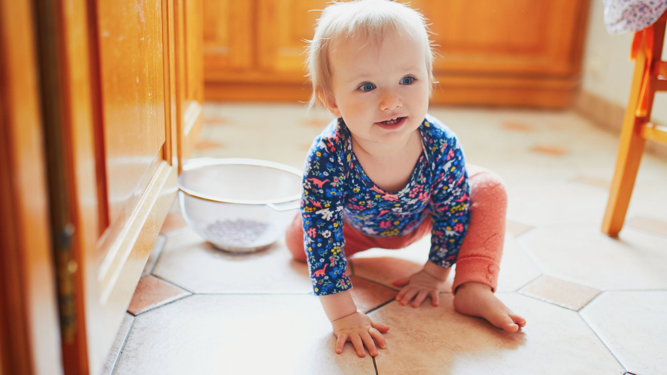 Kleinkind sitzt fröhlich auf dem Küchenfußboden.