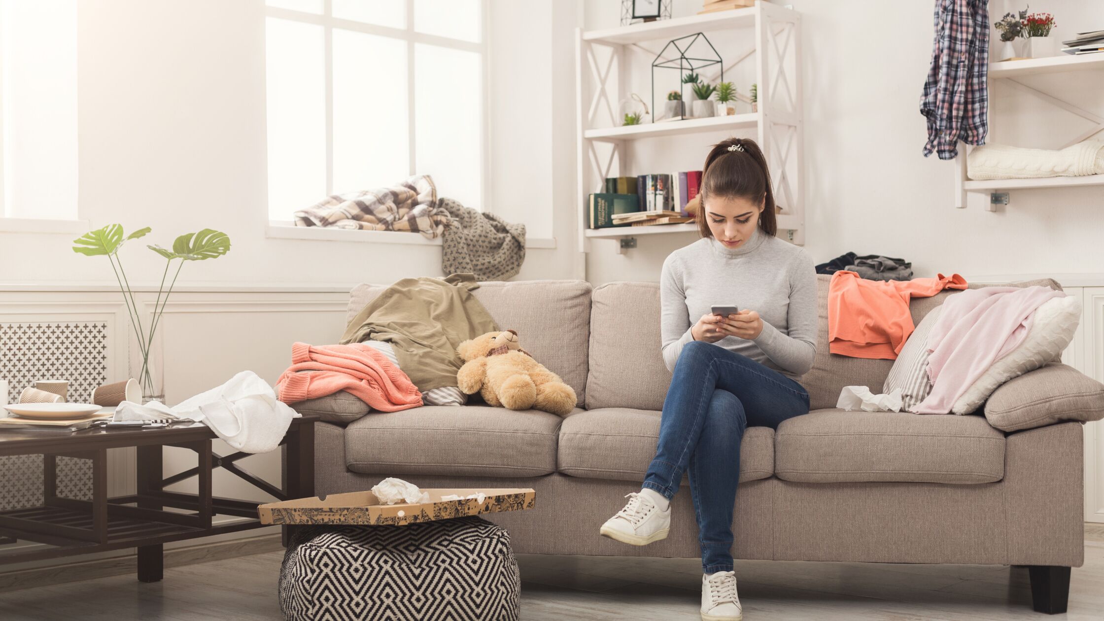 Die erste gemeinsame Wohnung: Umzugstipps fürs Zusammenziehen Junge Frau sitzt in chaotischem Wohnzimmer auf der Couch