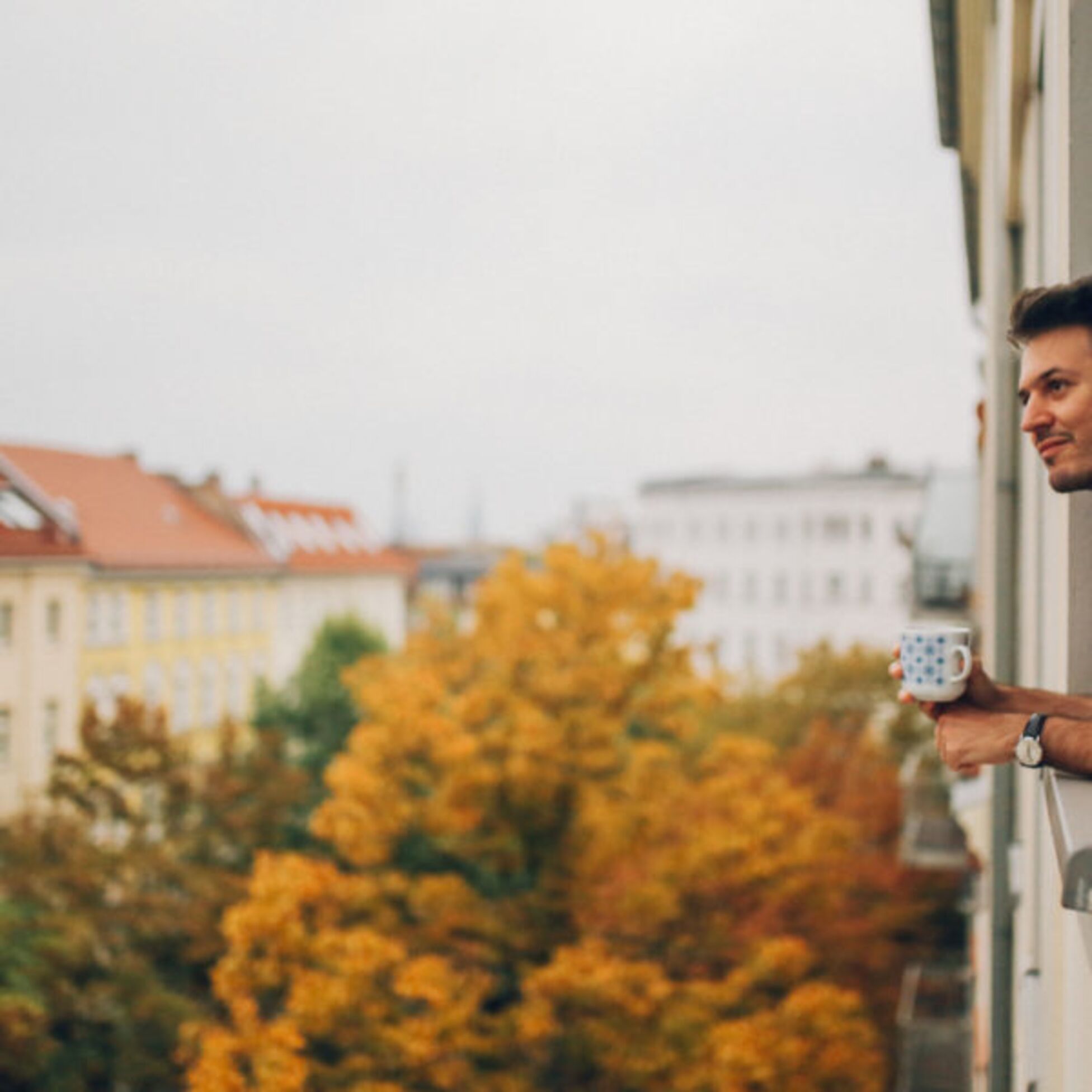 Junger Mann schaut aus dem Fenster eines größeren Wohnhauses