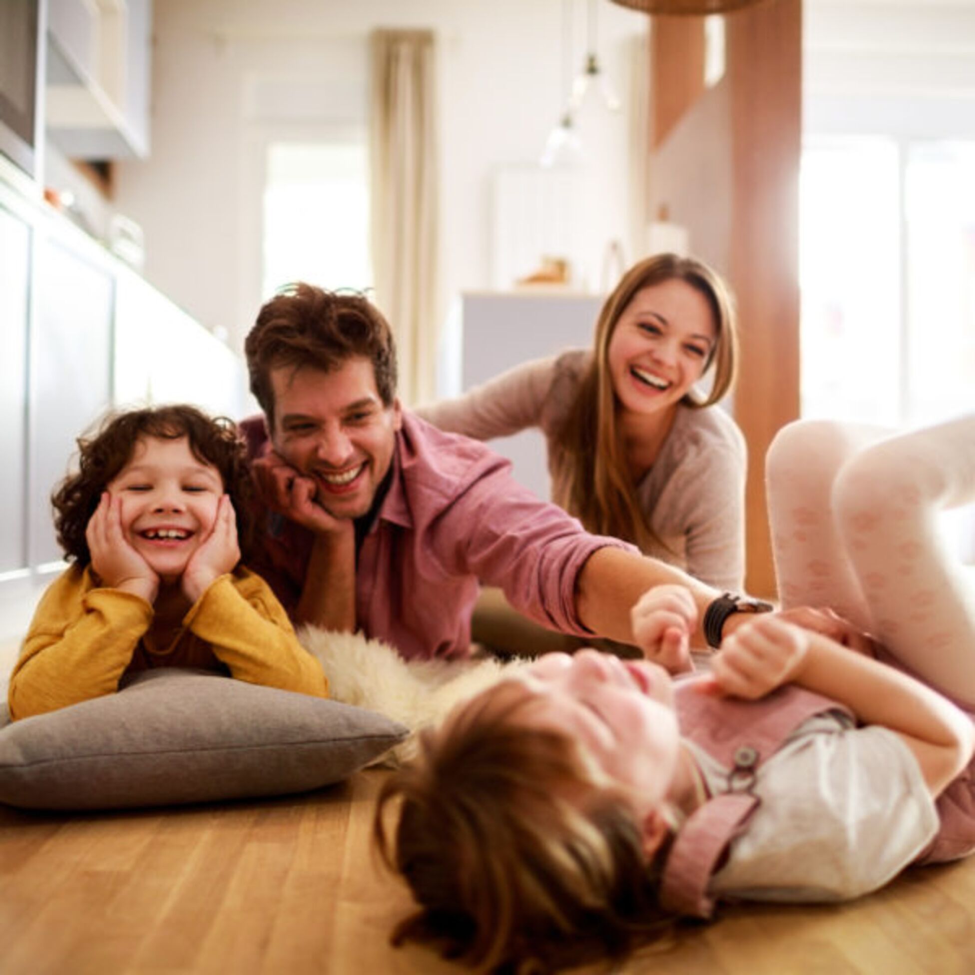 Junge Familie spielend und lachend auf dem Boden ihrer Wohnung