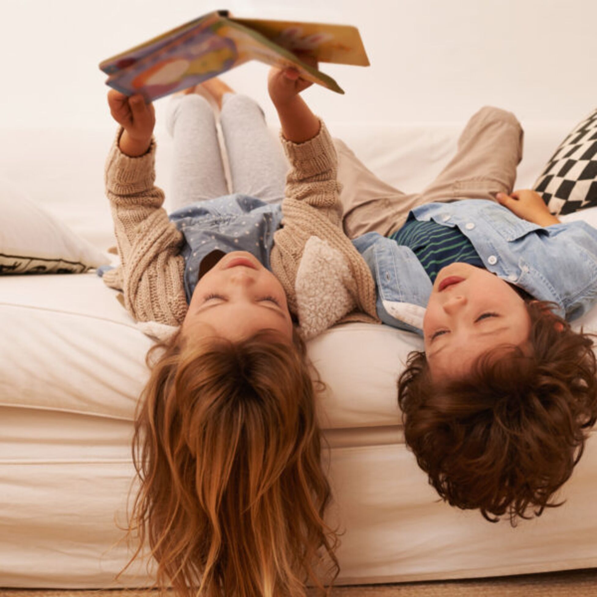 Zwei Kinder liegen auf einem Bett und lesen ein Buch