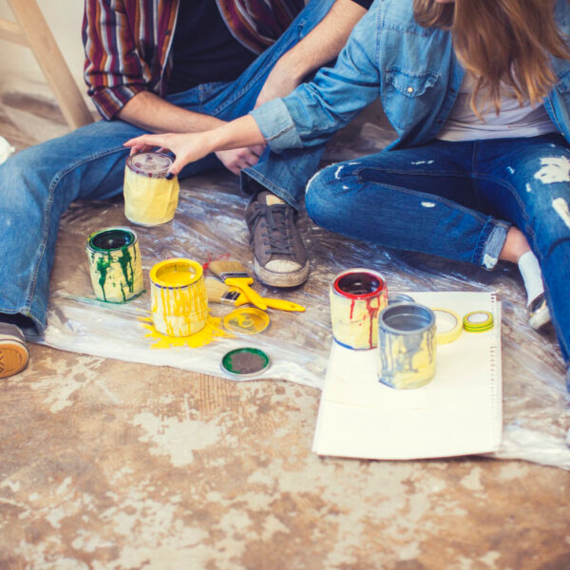 Junges Paar sitzt auf dem Boden zwischen leeren Farbeimern und Farbdosen