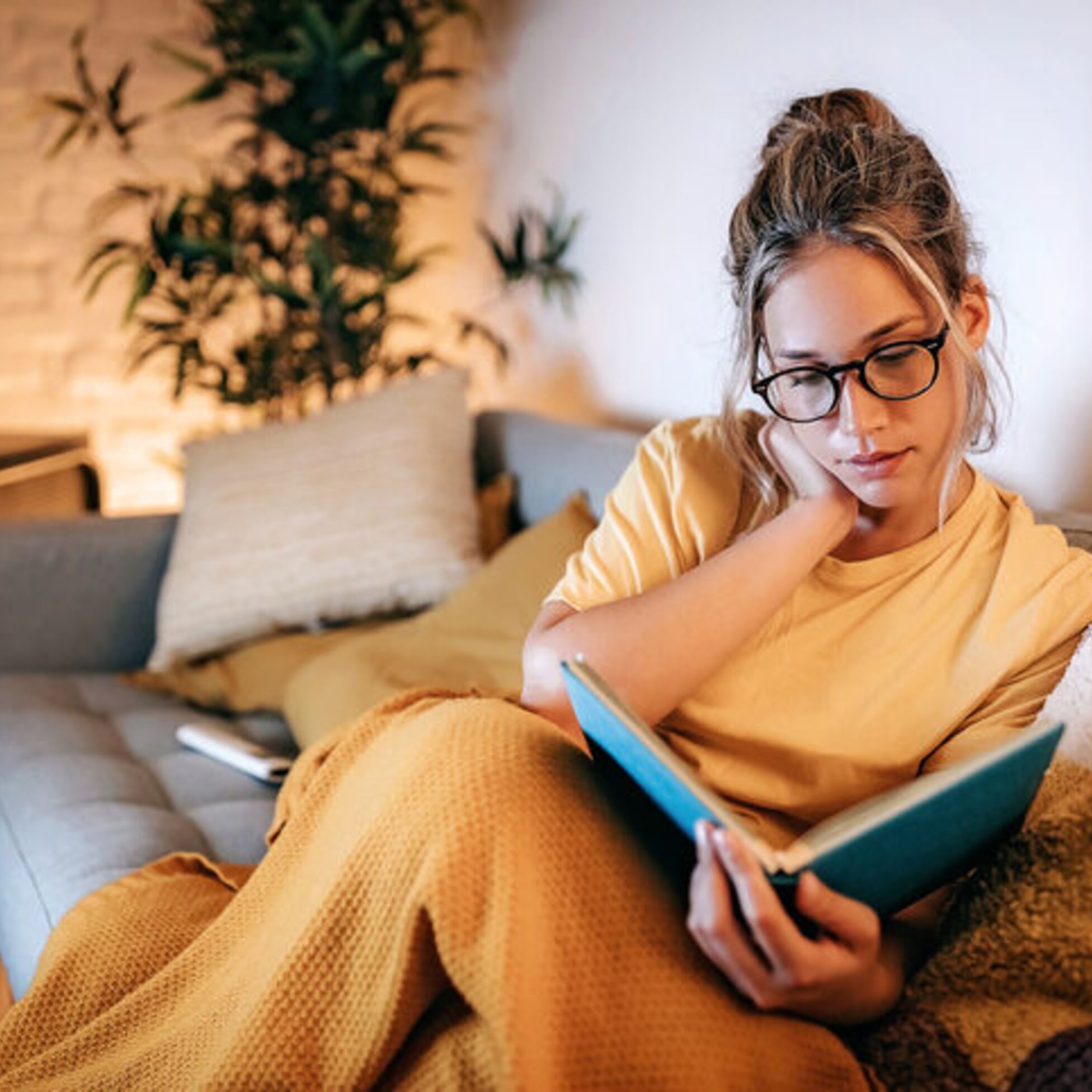 Frau liest Buch in gemütlichem Wohnzimmer