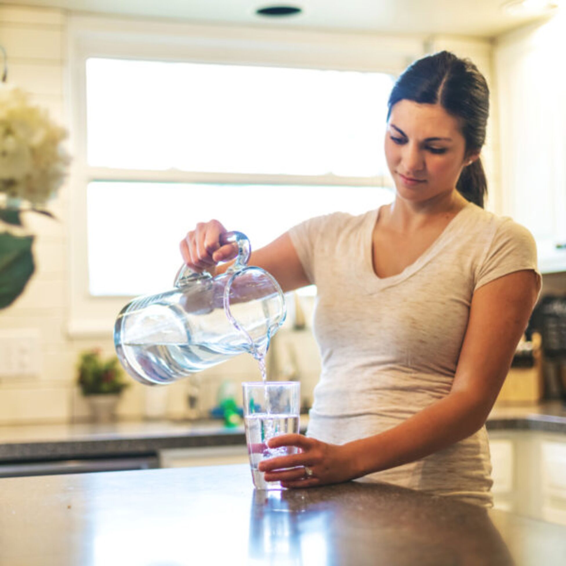 Frau schüttet Trinkwasser aus Karaffe in Glas