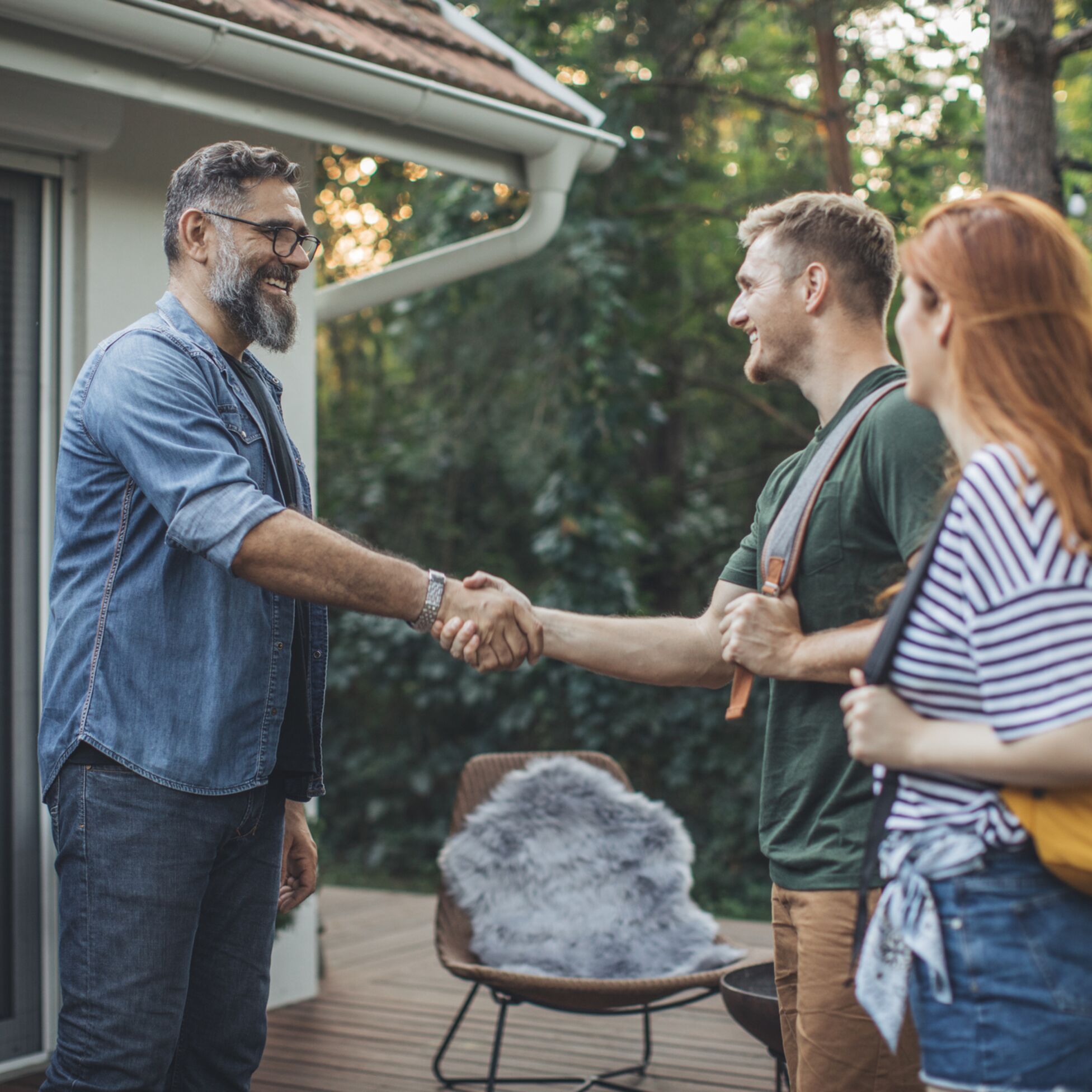 Ein Mann begrüßt ein Paar vor seinem Haus